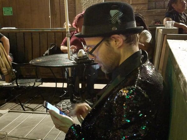 Charles Sadler on his phone while wearing a black sequin jacket and a stylish hat, 2019.